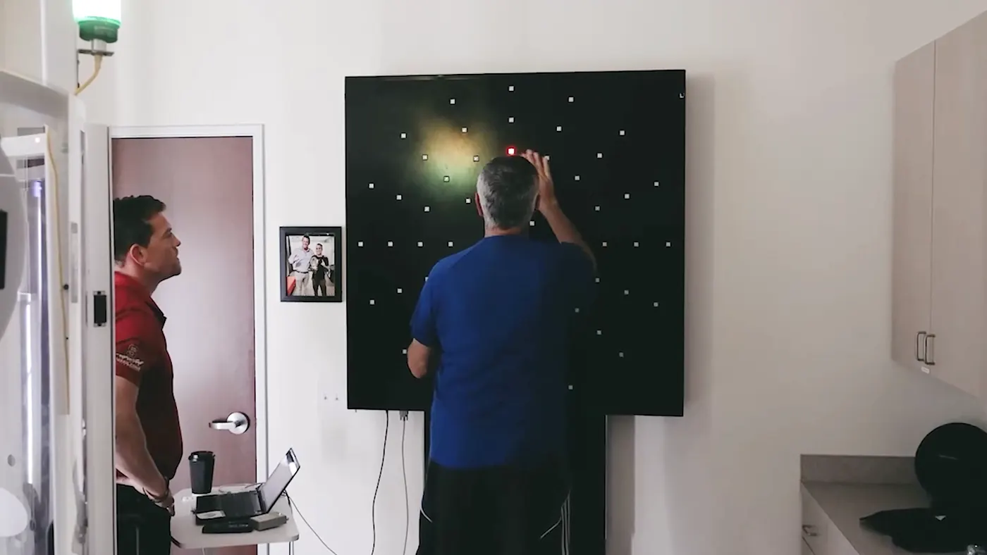 An athlete striking lit targets on the DynaVision board while Dr. McWhorter observes
